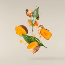 Fresh turmeric root with powder and green leaves falling in the air isolated on pink background Fresh turmeric root with powder and green leaves falling in the air isolated on pink background