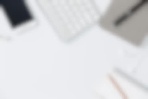 Mobile devices on a desk Cell phone, key board, ear phones and notebook arranged side by side on a white desk