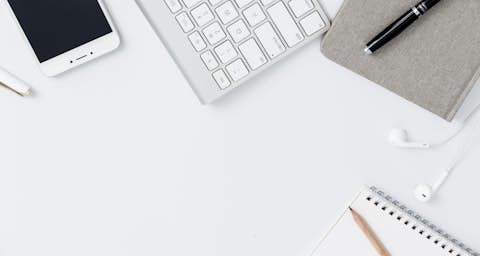 Mobile Geräte auf einem Schreibtisch Mobiltelefon, Tastatur, Kopfhörer, Notizbuch, Block und Stift auf einem weißen Schreibtisch