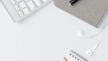 Mobile Geräte auf einem Schreibtisch Mobiltelefon, Tastatur, Kopfhörer, Notizbuch, Block und Stift auf einem weißen Schreibtisch