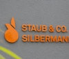 Company Logo STAUB & CO. - SILBERMANN GmbH Orange company Logo STAUB & CO. - SILBERMANN GmbH on grey wall