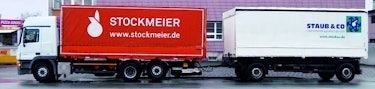 LKW mit Anhänger LKW, dessen Plane für STOCKMEIER wirbt, mit einem Anhänger, der mit dem Logo der Staub & Co. beschriftet ist.