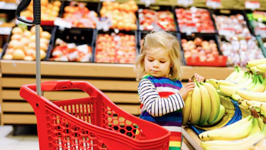 Small child in a shopping trolley putting bananas into the trolley in the fruit department. Small child in a shopping trolley putting bananas into the trolley in the fruit department.