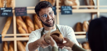 Shot of a cheerful salesman handing a woman fresh bread in the bakery. Shot of a cheerful salesman handing a woman fresh bread in the bakery.
