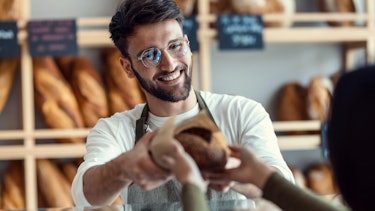 Shot of a cheerful salesman handing a woman fresh bread in the bakery. Shot of a cheerful salesman handing a woman fresh bread in the bakery.