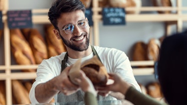 Shot of a cheerful salesman handing a woman fresh bread in the bakery. Shot of a cheerful salesman handing a woman fresh bread in the bakery.