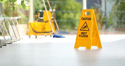 Cleaned floor with "Caution - wet floor" sign and cleaning machine in the background Cleaned floor with "Caution - wet floor" sign and cleaning machine in the background