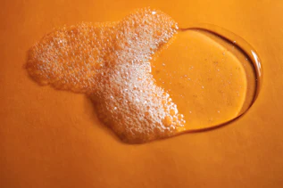Flüssiges Duschgel mit Schaum auf orangener Oberfläche Flüssiges Duschgel mit Schaum auf orangener Oberfläche