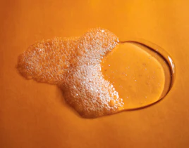 Flüssiges Duschgel mit Schaum auf orangener Oberfläche Flüssiges Duschgel mit Schaum auf orangener Oberfläche