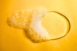 Flüssiges Duschgel mit Schaum auf gelber Oberfläche Flüssiges Duschgel mit Schaum auf gelber Oberfläche