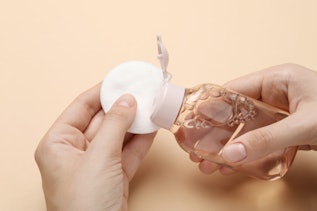 Woman pouring micellar water from bottle onto cotton pad Woman pouring micellar water from bottle onto cotton pad