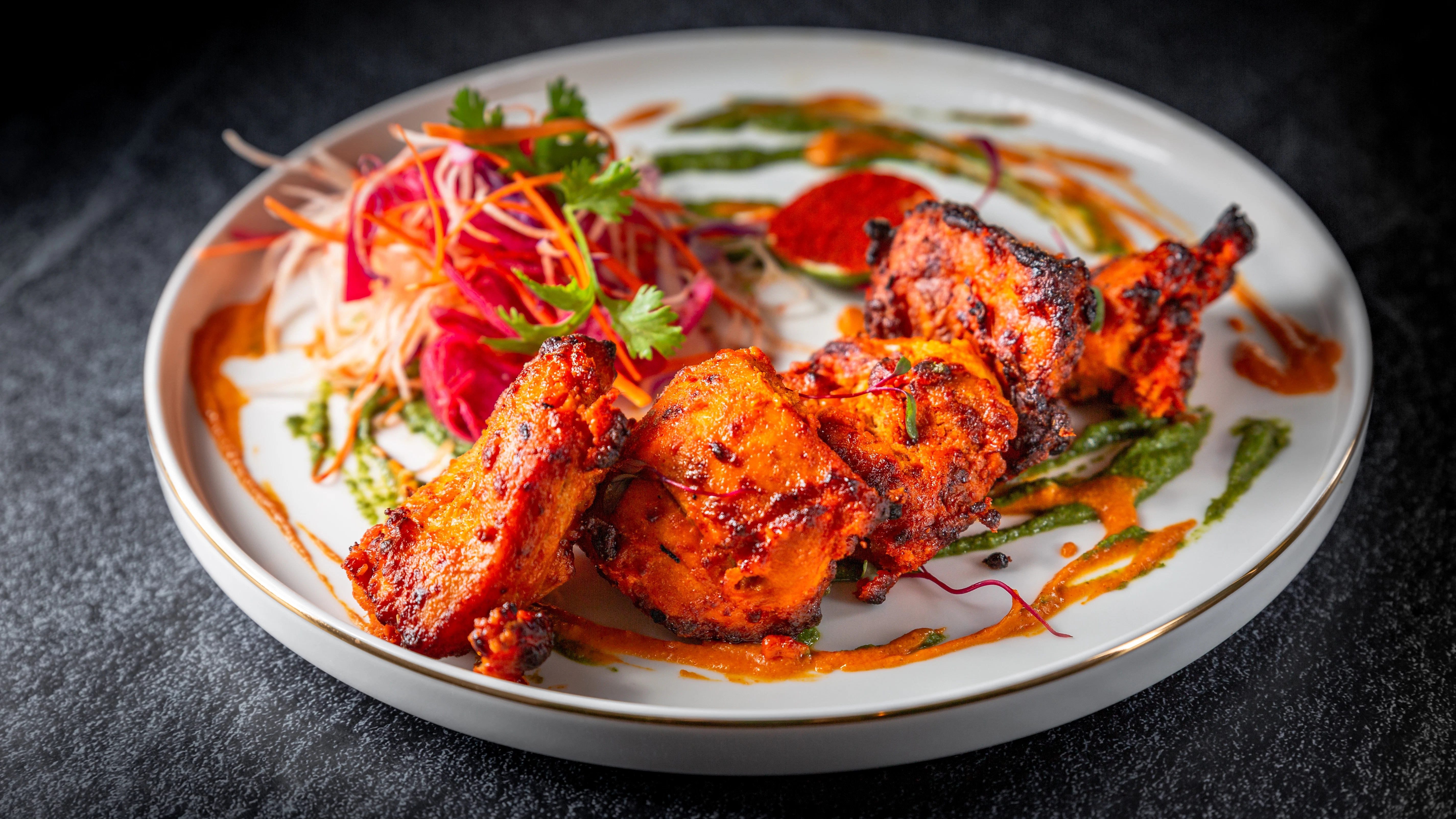 Grilled chicken wings with colorful vegetable garnish Several grilled chicken wings are arranged on a white plate with shredded vegetables and colorful sauce. The dish is presented on a dark table surface.