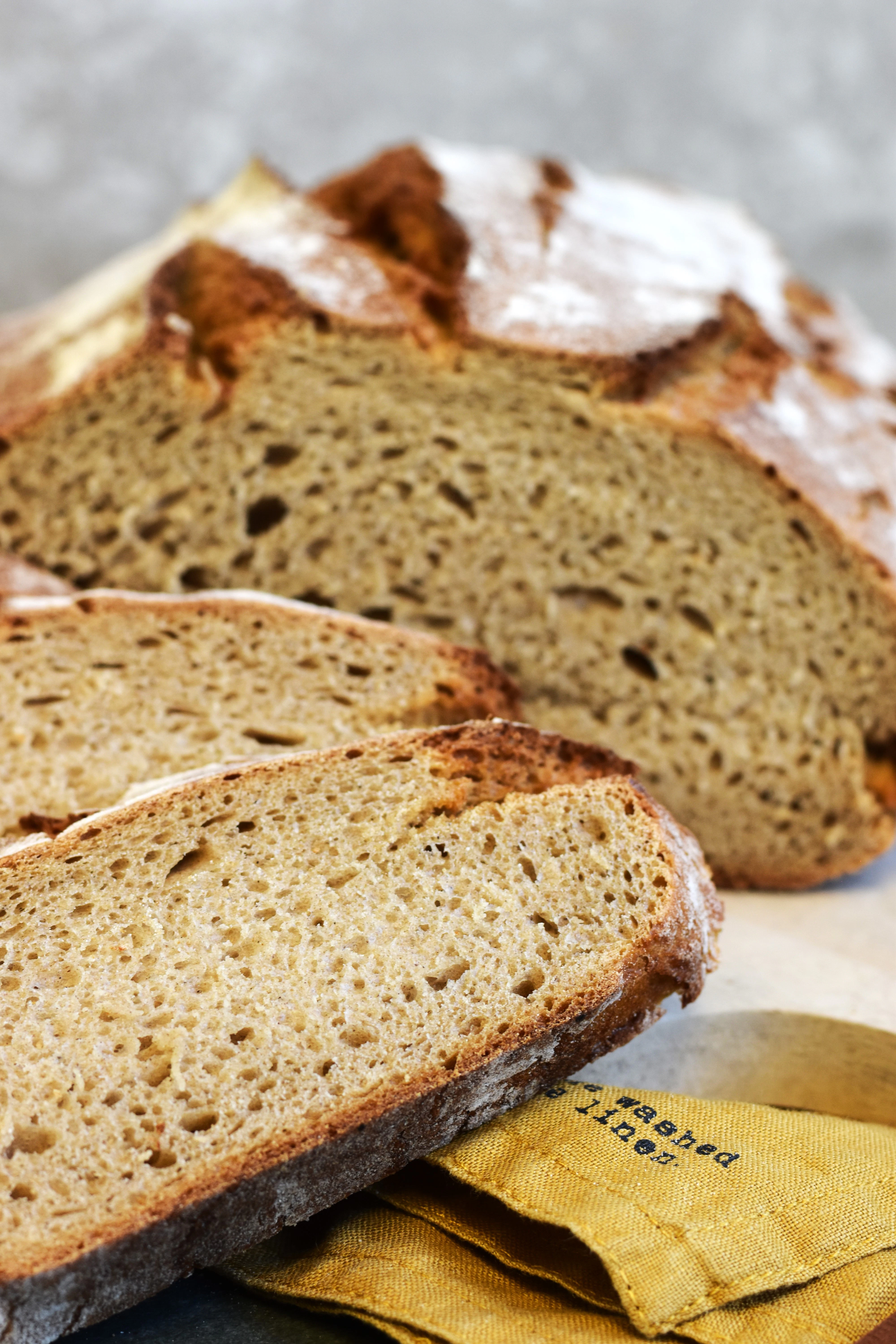 Rustic bread loaf with sliced pieces A freshly baked bread loaf is cut into slices, showing a soft crumb and crispy crust. The bread is placed on a cloth with a blurred background.