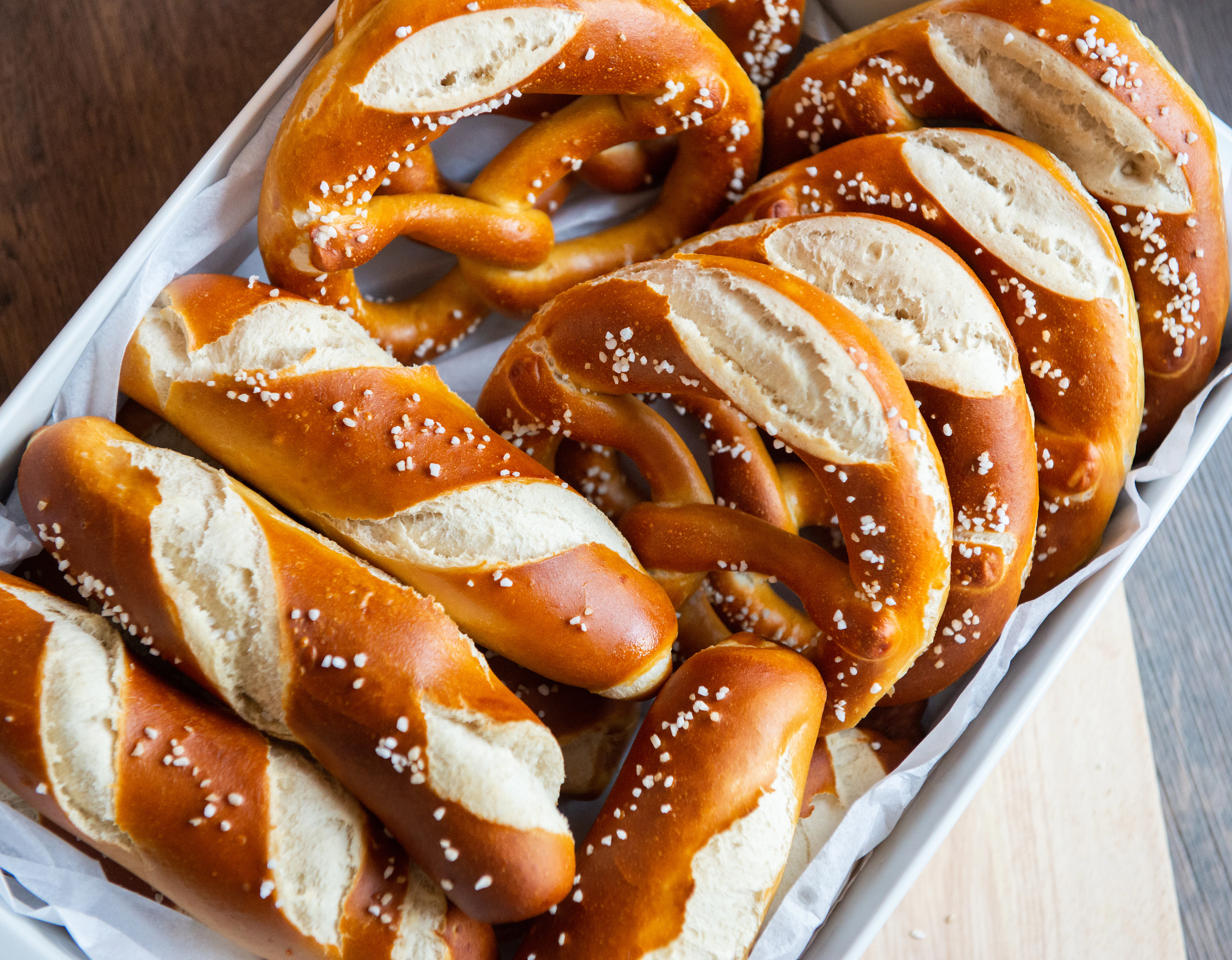 Soft pretzels with coarse salt Several golden-brown pretzels with coarse salt are arranged in a basket with paper lining. The pastries have a glossy surface and soft interior.