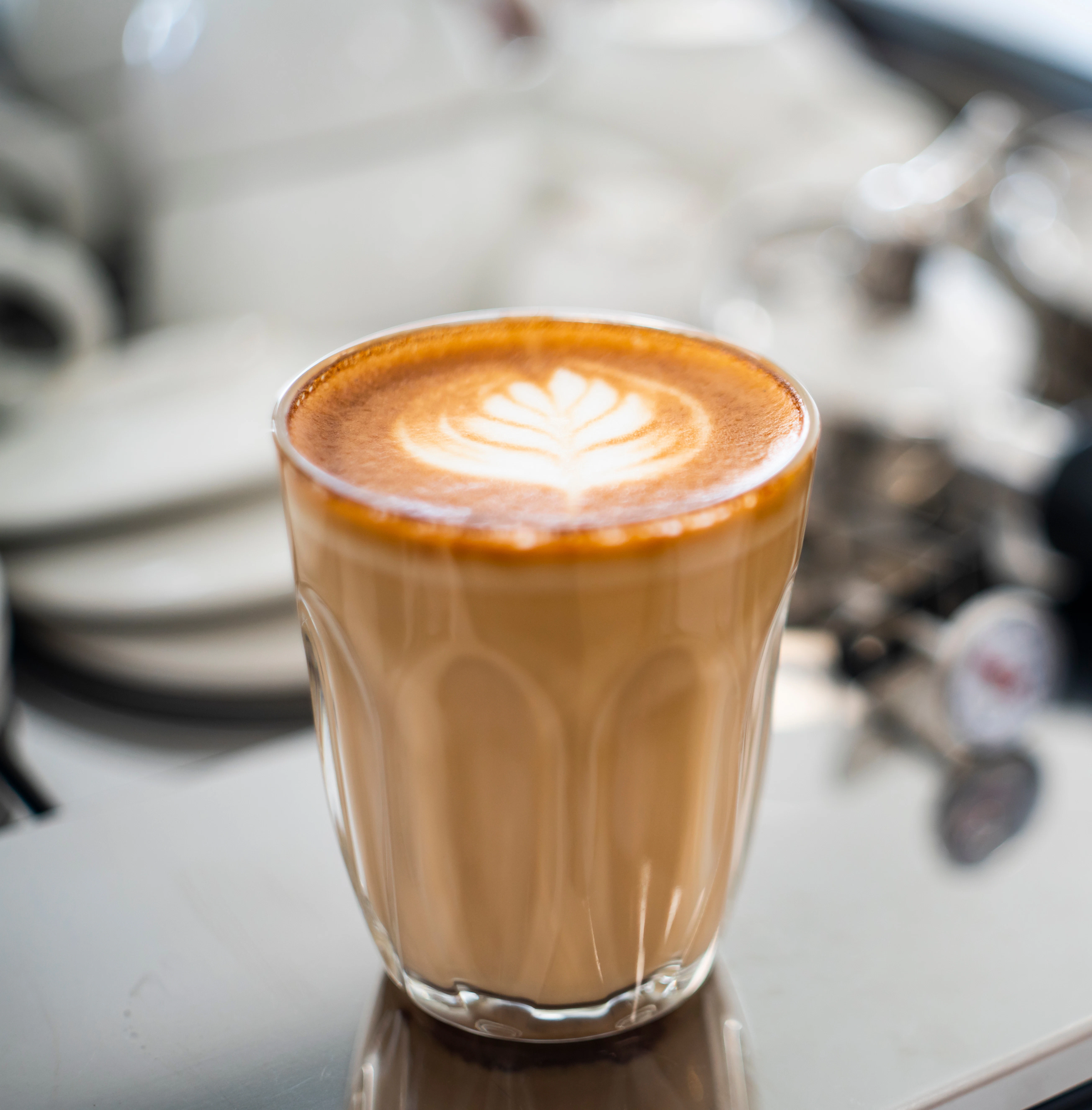 Fresh latte with decorative milk foam A glass of latte stands on a coffee machine with decorative milk foam on top. The background is softly blurred.