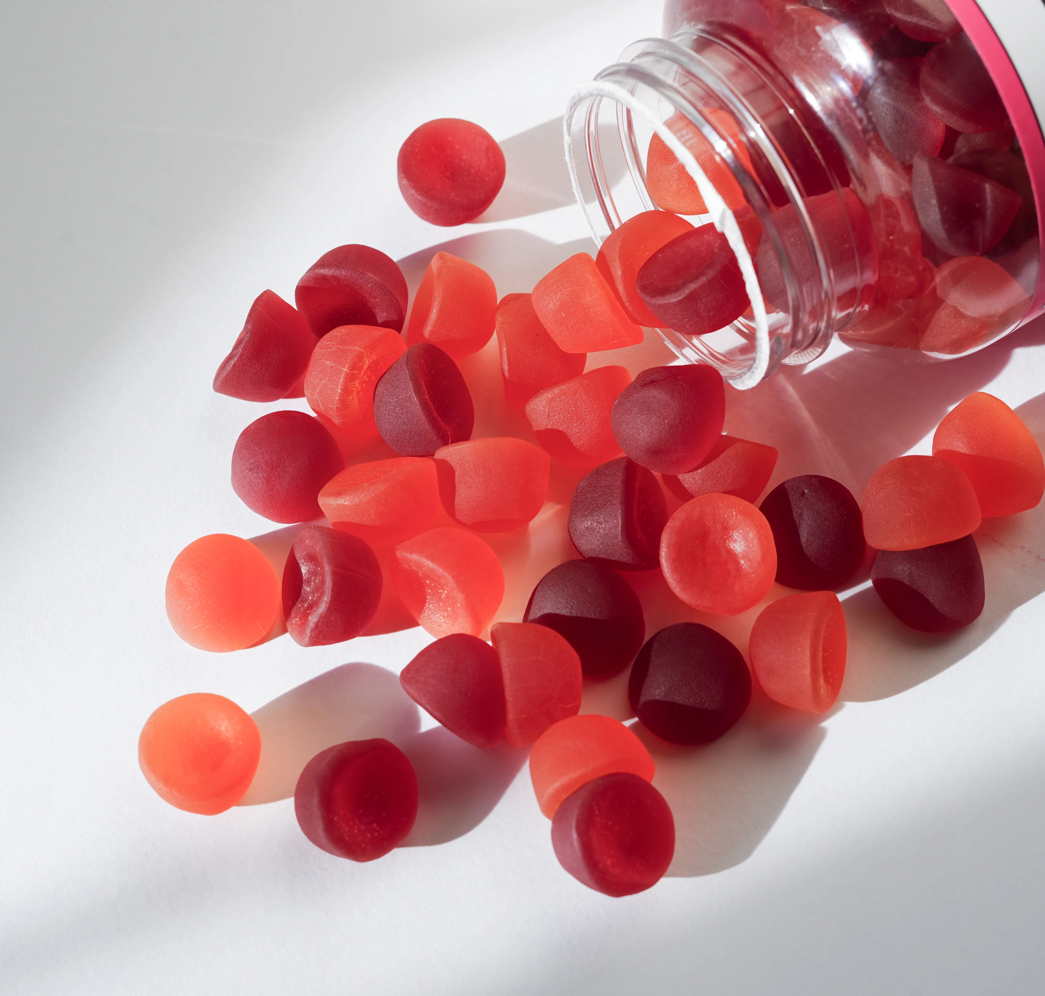 Red gummy spilling from container Red gummies are scattered across a light surface from an open container. The gummies vary in shape and size.