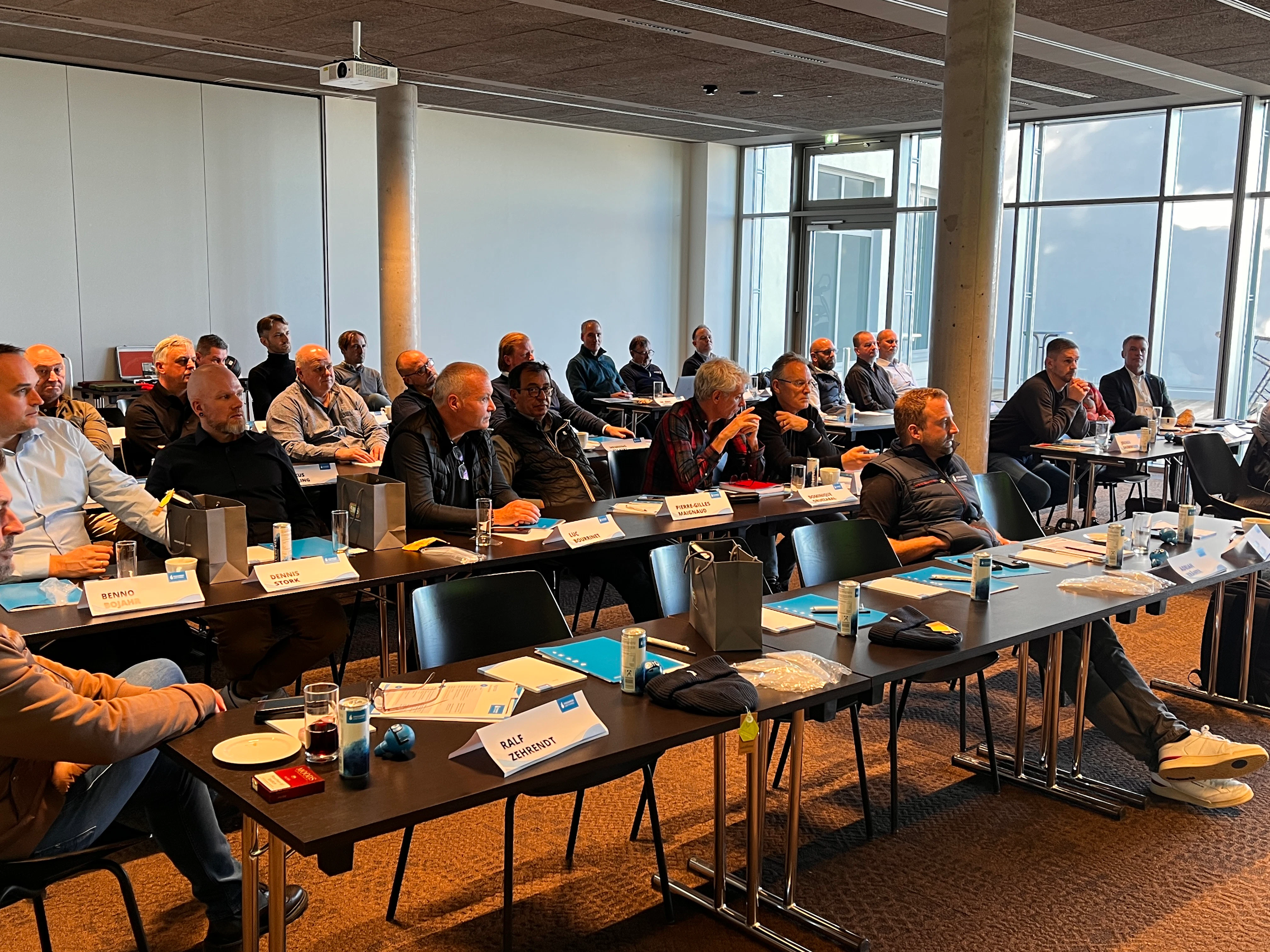 Teilnehmende während einer Präsentation Teilnehmende sitzen an ihren Tischen und folgen der Präsentation