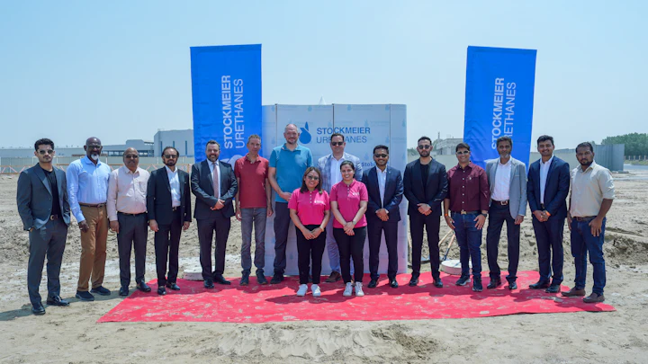 Teilnehmende stehen auf einem roten Teppich in der Wüste vor einer Logo-Wand