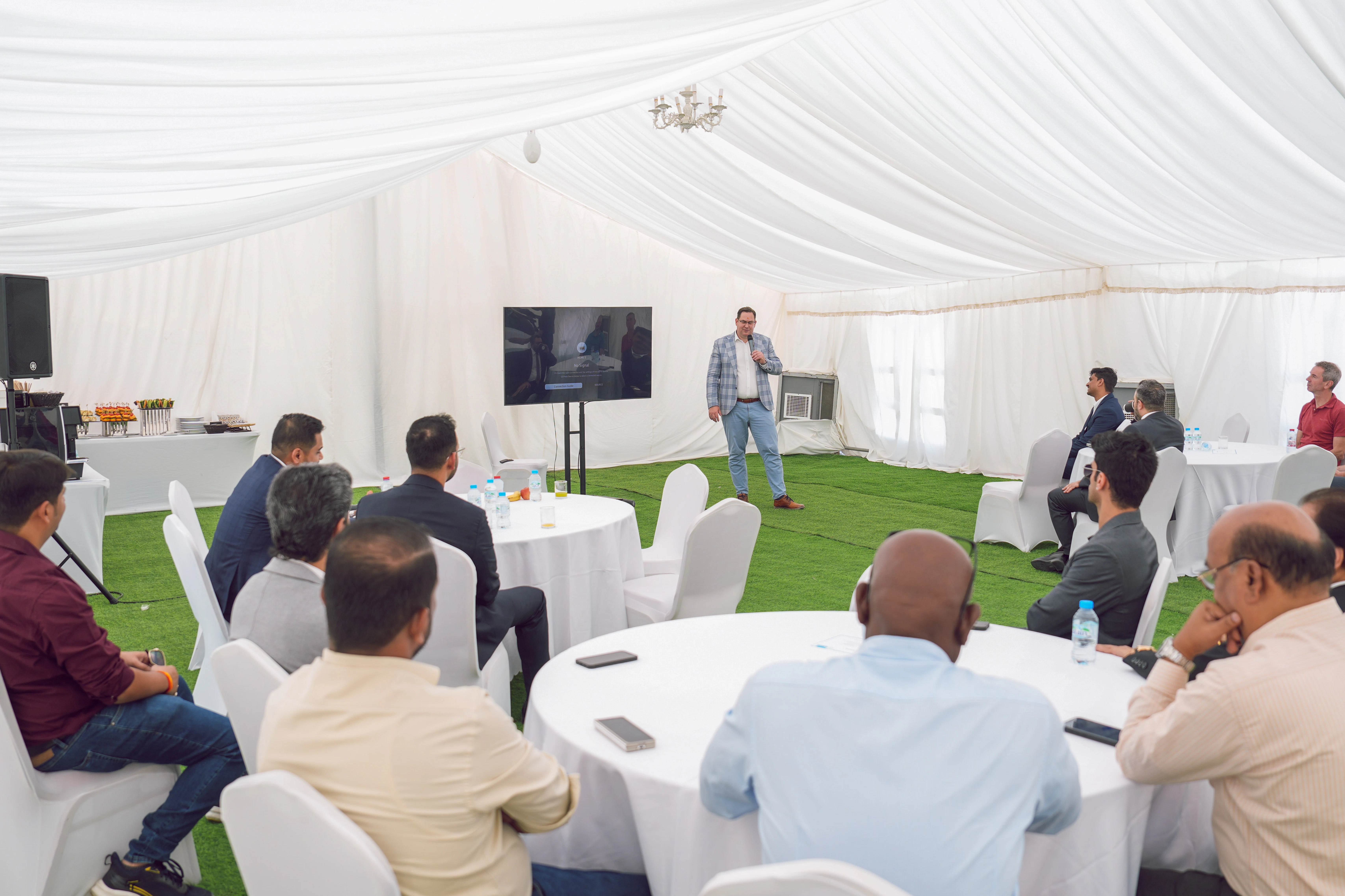 Gäste hören CEO Markus Lamb zu während der eine Rede hält Menschen sitzen um runde Tische und hören einer Rede zu