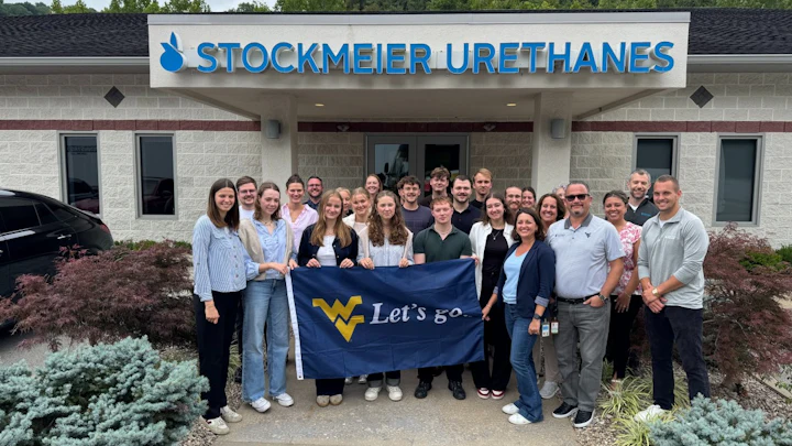 WVU and FH-Münster University of Applied Sciences Student in a group photo with employees at STOCKMEIER Urethanes USA holding a "Lets Go" WV flag