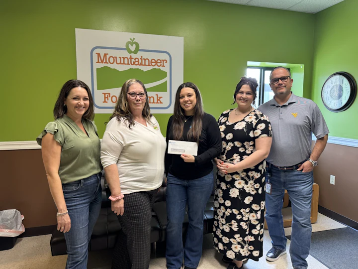 STOCKMEIER Urethanes USA employees with Mountaineer Food Bank employees handing over a check standing in the lobby. There are three four women and one man.