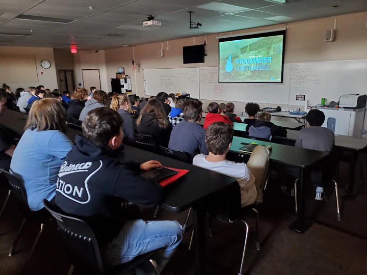 Kinder sitzen an Tischen und schauen einer Präsentation über STOCKMEIER Urethanes zu