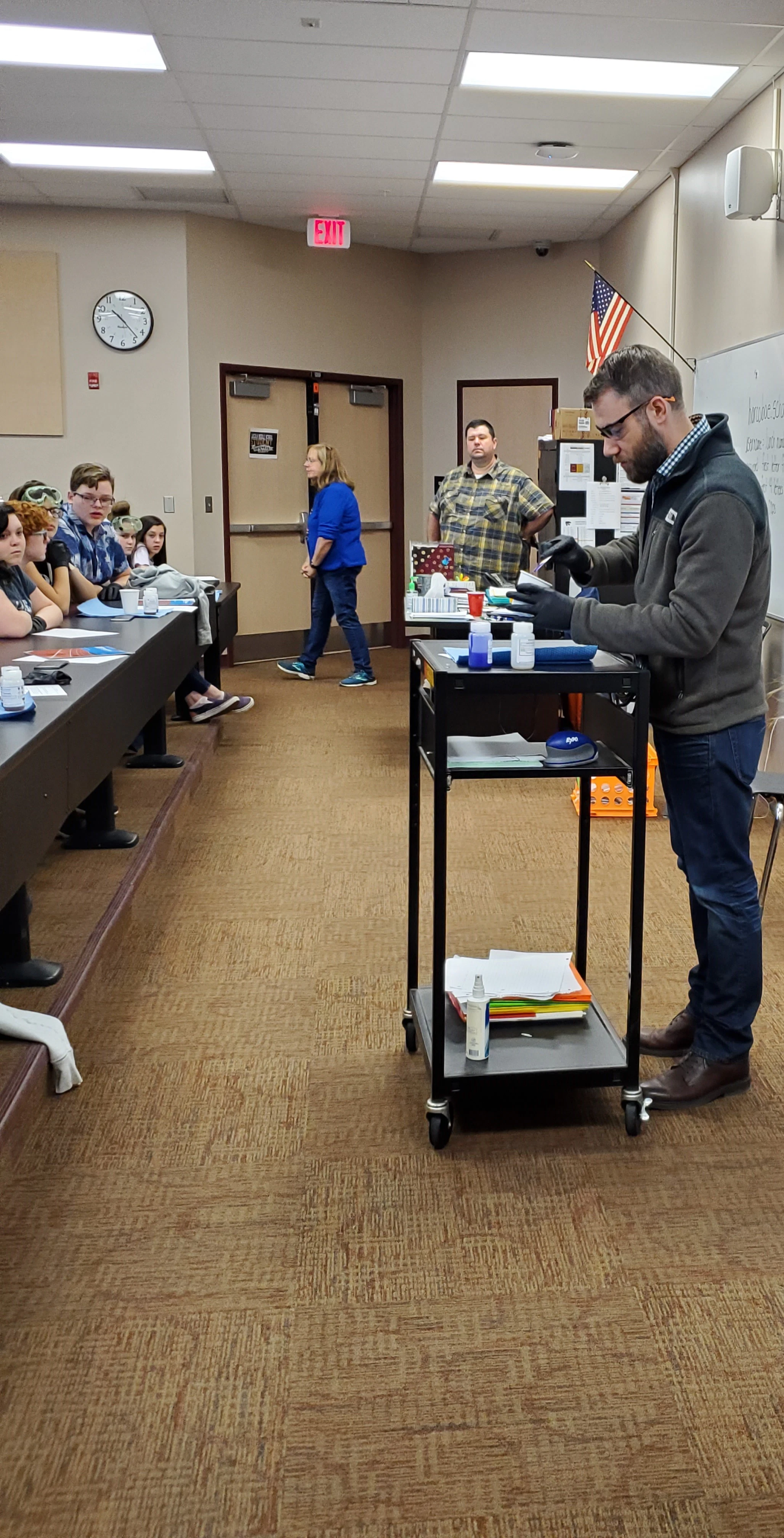 STOCKMEIER Urethanes kooperiert mit WVMA 7 Mann steht mit einer Schutzbrille und Schutzhandschuhen an einem Pult vor Schülern und führt ein Experiment durch